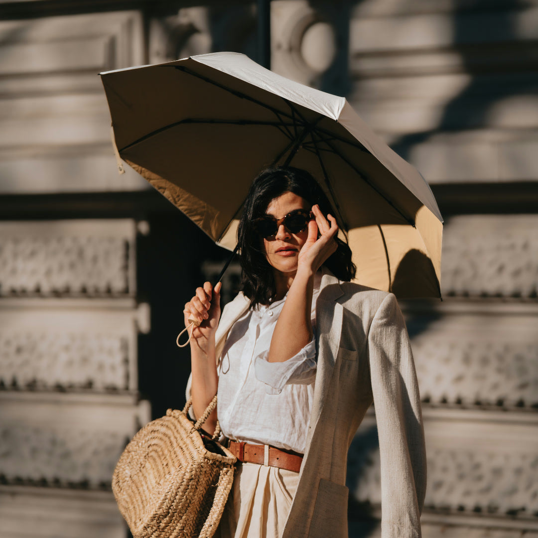 Woman in linen holding the open Sunbarry Cool Shader in Desert & Taupe – UV umbrella with wooden handle and taupe-cream two-tone, certified UPF 50+#Color_Desert & Taupe