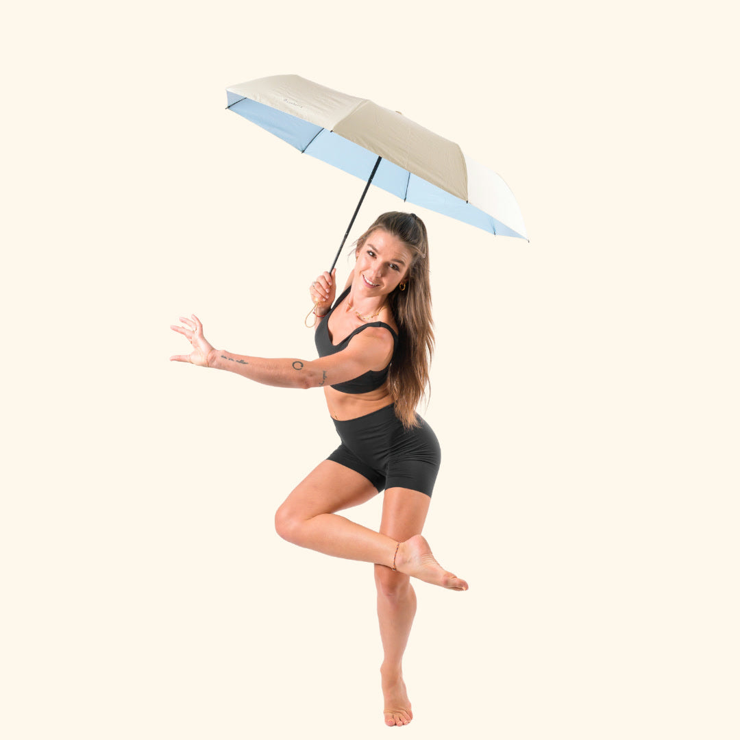 Woman posing with the open Sunbarry Cool Shader in Butter & Sky – UV umbrella with butter-cream and sky-blue panels, wooden handle, certified UPF 50+#Color_Butter & Sky