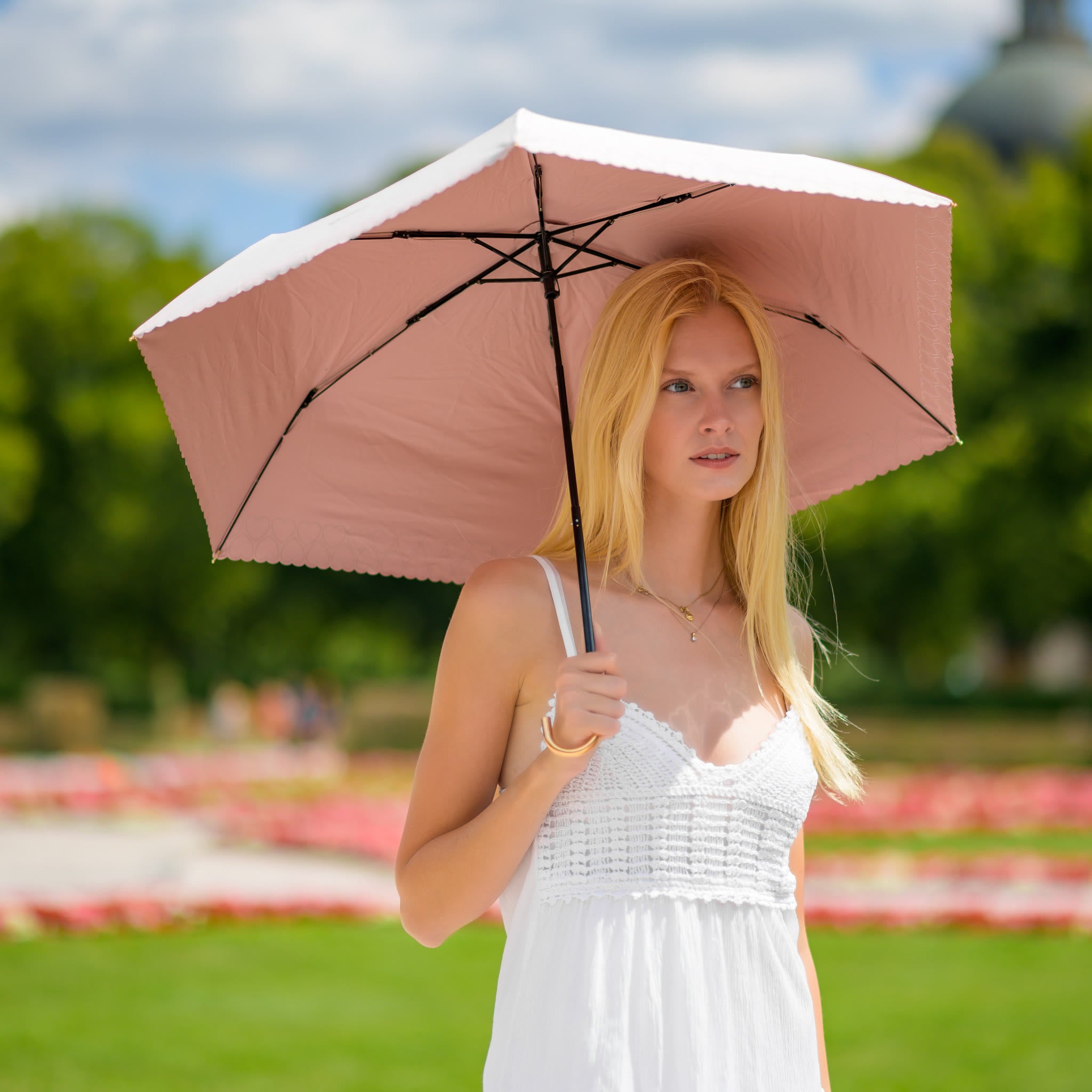Frau mit Sunbarry Romantic Breezer Blush Rosé im Park – UV-Sonnenschirm mit Herzbordüre und Goldgriff#Farbe_Blush Rosé
