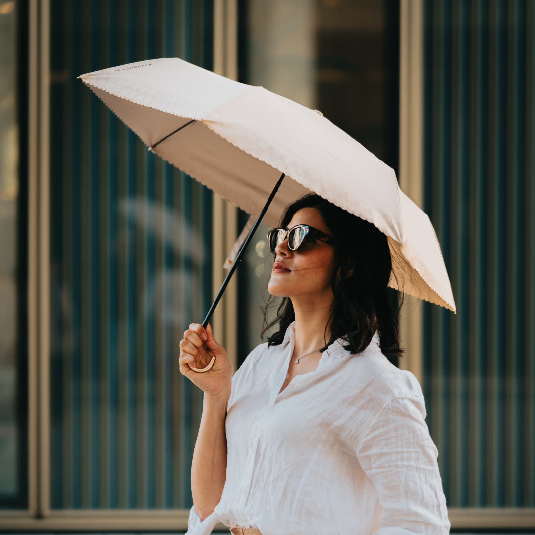 Woman with the Sunbarry Romantic Breezer in Pearl Beige in the city – UV umbrella with heart trim and gold handle#Color_Pearl Beige